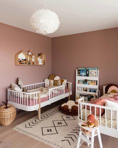 a baby's room with two white cribs and pink walls