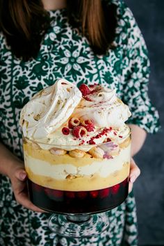 a woman holding a cake with whipped cream and raspberries on top in her hands