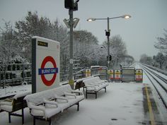 benches covered in snow next to train tracks and street lights on a snowy day,