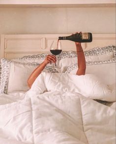 a person laying in bed with a glass of wine on their head and one hand holding a bottle