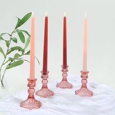 three pink candles sitting next to each other on a white cloth with a plant in the background