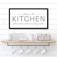 a kitchen sign hanging on the wall above a shelf filled with cups and mugs