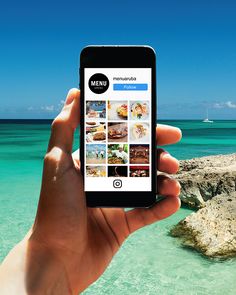 someone holding up their cell phone to take a picture of the beach and ocean in front of them