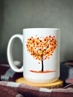 a white coffee mug with an orange tree painted on the front and side, sitting on a wooden coaster