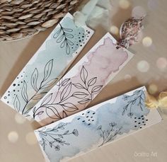 two tags with watercolor designs on them sitting next to a basket and some other items