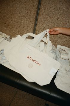 a person holding a white bag with the word & tradition on it sitting on a black leather bench