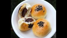 three buns with black seeds on them sitting in a white bowl, one is cut in half and the other has been eaten