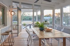 a dining room table with chairs and a bowl of fruit on it in front of large windows