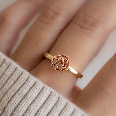 a close up of a person's hand wearing a gold ring with a rose on it