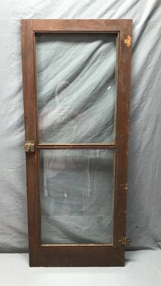 an old wooden window sitting on top of a white cloth covered wall in front of a gray backdrop