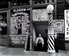 an old black and white photo of a man standing in front of a barbershop