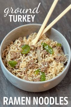 a white bowl filled with noodles and meat on top of a wooden table next to chopsticks