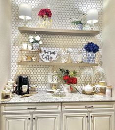 a counter with flowers and tea cups on it in a room that has white hexagonal tiles