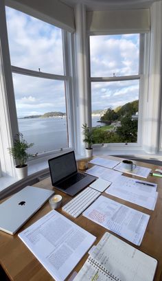 an open laptop computer sitting on top of a wooden desk next to two large windows