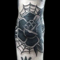 a black and white photo of a spider web with a rose tattoo on it's leg