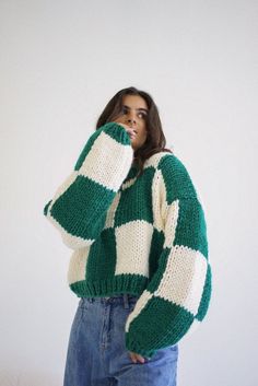 a woman in a green and white sweater is holding her hand to her face while standing against a wall