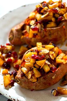 two baked potatoes with cranberry sauce and nuts on a white plate, ready to be eaten