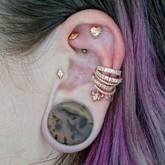 a woman with purple hair wearing gold ear cuffs and piercings on her left ear