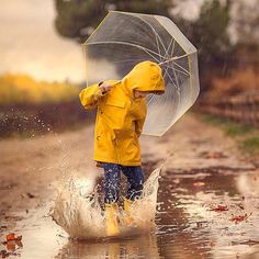 a person in yellow raincoat and blue jeans walking through water with an open umbrella