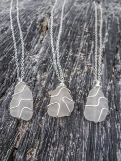 three silver necklaces sitting on top of a piece of wooden table next to each other