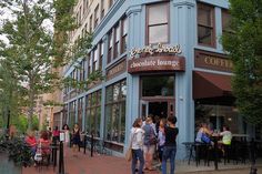 people are standing outside of a coffee shop on the sidewalk in front of a building