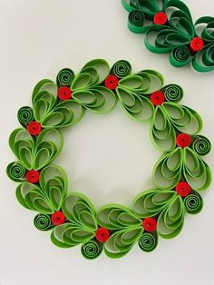 an origami christmas wreath with red buttons and green leaves on it, next to a smaller one made out of rolled paper