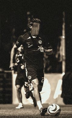 a black and white photo of a man kicking a soccer ball on a field with other men in the background