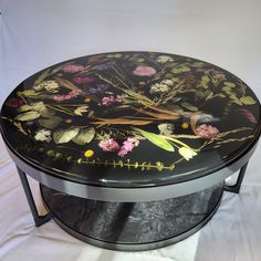 a black table with flowers painted on the top and silver trimmings around it