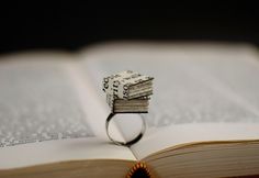 a stack of money sitting on top of an open book next to a silver ring