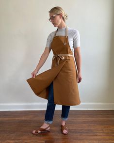 a woman wearing an apron and glasses standing on a hard wood floor in front of a white wall