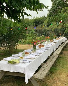 a long table is set up with plates and glasses for an outdoor dinner in the garden