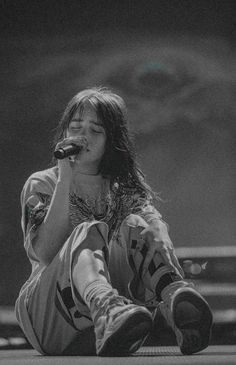 a woman sitting on the ground while holding a microphone in her hand and singing into a mic