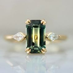 an emerald and diamond ring with three diamonds on the side, set in yellow gold