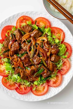 a white plate topped with meat and veggies next to chopsticks on top of rice