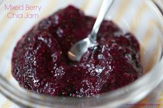 a spoon in a bowl filled with mixed berry chia jam on a yellow and white tablecloth