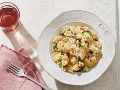 a white bowl filled with pasta and spinach on top of a pink napkin next to a fork