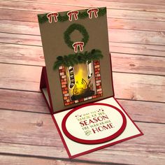 a christmas card with a fireplace and wreath on it, sitting on top of a wooden table