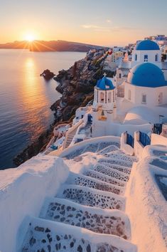 the sun is setting over some white buildings by the water with blue domes on them