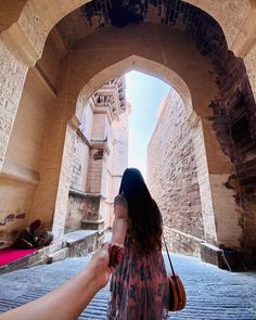 a woman holding the hand of a man who is walking through an arch in a stone building