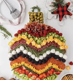 a platter filled with fruit and vegetables on top of a white table next to other food