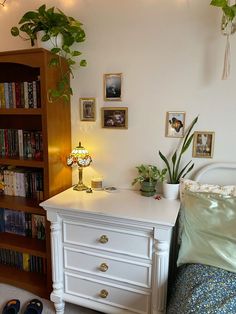 a bedroom with a bed, book shelf and plant on the nightstand next to it