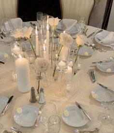 a white table topped with lots of plates and silverware covered in flowers next to candles