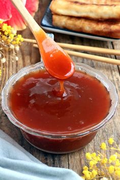 a spoon full of ketchup sitting on top of a wooden table next to some yellow flowers