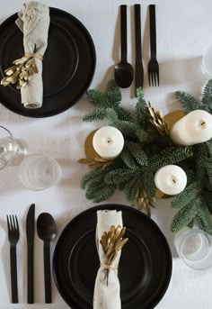 the table is set with black plates, silverware and candlesticks for christmas