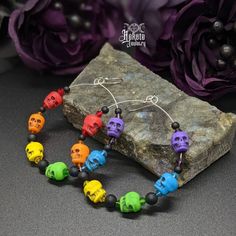 the colorful skull beaded bracelet is next to a rock and purple flowers on it