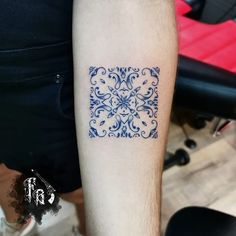 a blue and white tattoo design on the left inner arm, with an intricate square in the middle