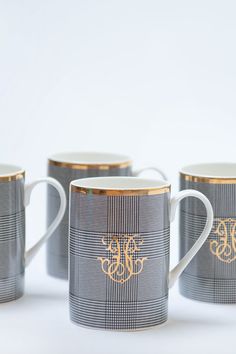 four coffee mugs with monogrammed designs are lined up on a white surface