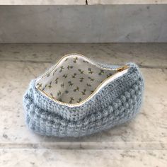 a knitted blue purse sitting on top of a marble counter next to a wall