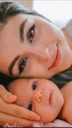 a woman holding a baby in her arms while laying on top of a bed next to it