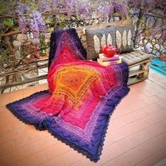 a crocheted blanket sitting on top of a wooden bench next to a potted plant